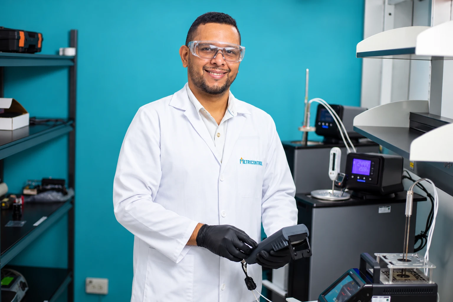 Técnico de METRILAB con lentes de seguridad y guantes sosteniendo un indicador junto a los equipos de calibración de temperatura